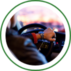 A driver grips a vehicle steering wheel as they drive at dusk. 